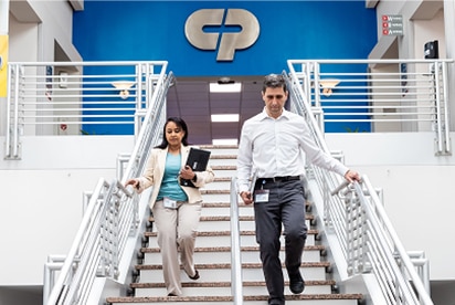 Zaposleni v podjetju Colgate-Palmolive se spuščajo po stopnicah, za njimi pa je na modri steni logotip podjetja Colgate-Palmolive.