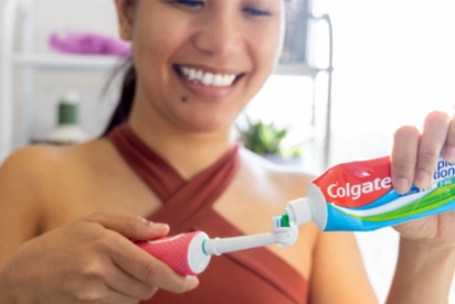 Ženska se smeji, medtem ko v kopalnici na zobno ščetko nanaša zobno pasto Colgate.